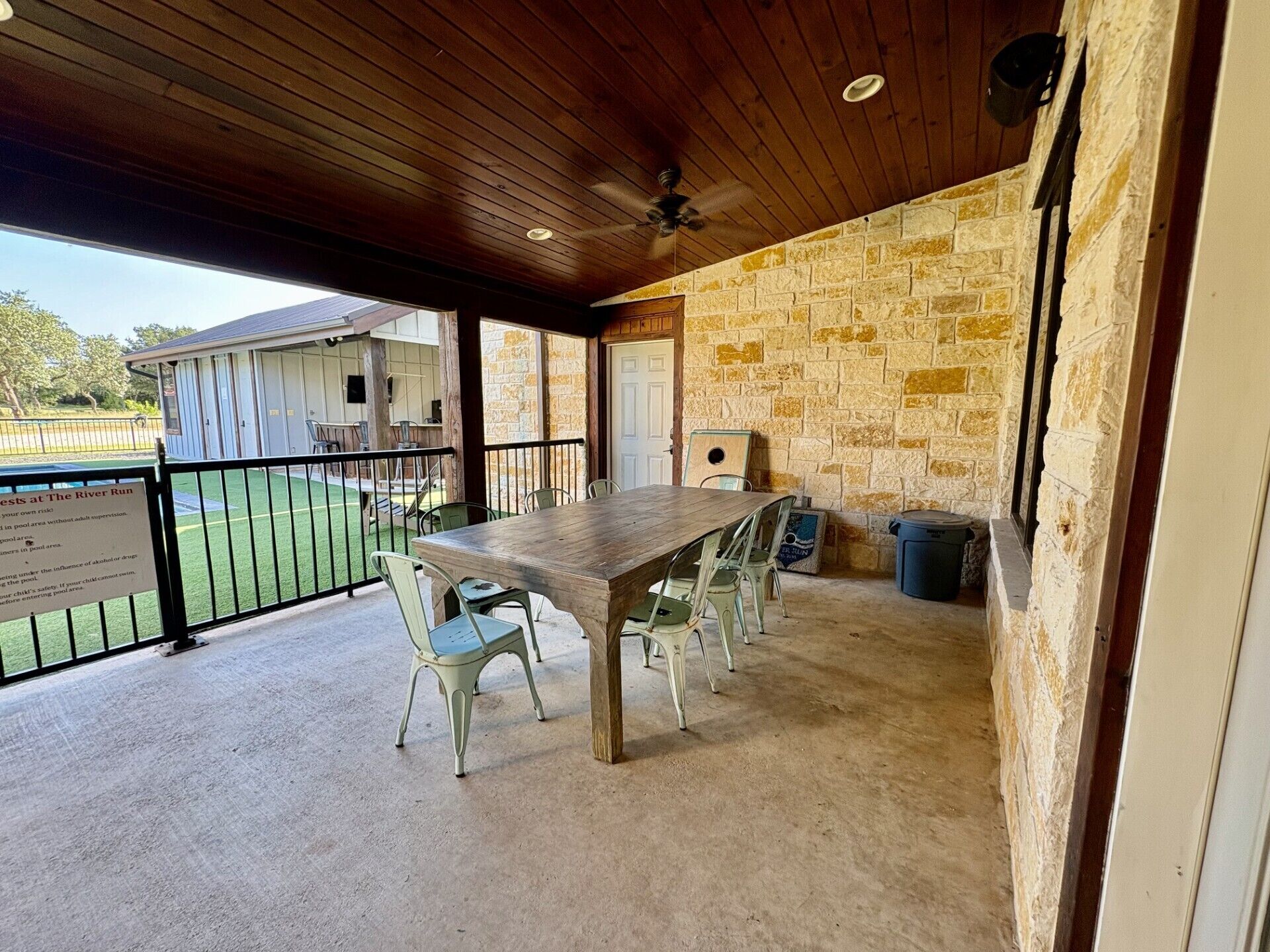 Un patio al aire libre con una mesa y sillas de madera, muros de piedra y vistas a una zona de piscina.