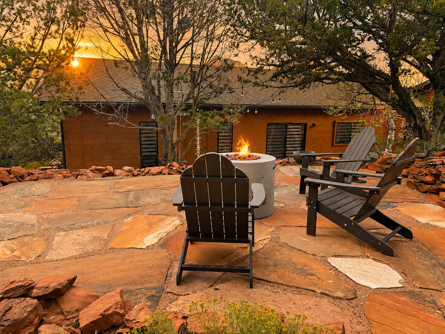 An outdoor patio with a fire pit, two Adirondack chairs, and a stone-tiled floor.