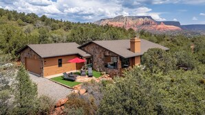 A two-story stone house with a stone chimney, a red umbrella, and a patio with outdoor furniture.