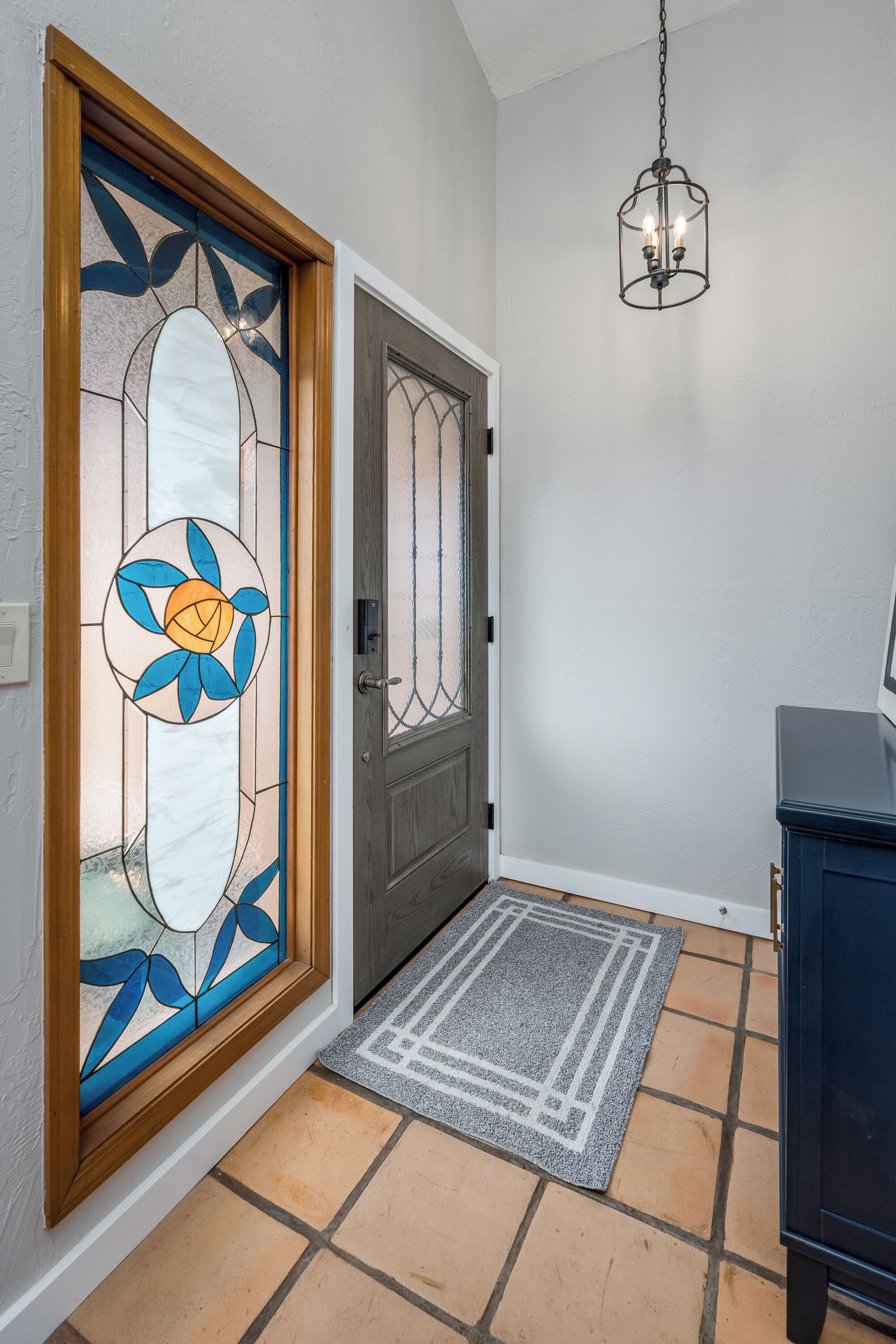 A foyer with a wooden-framed stained glass door, a grey mat, and a hanging light fixture.