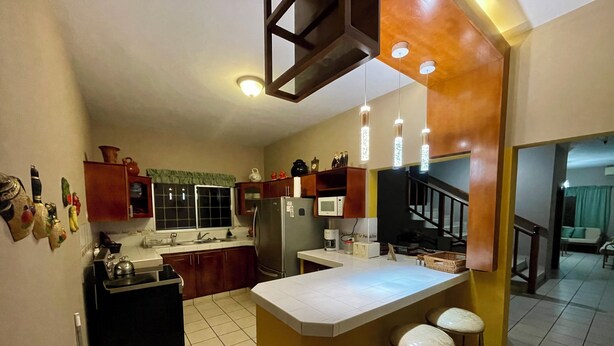 A kitchen with a central island, bar stools, a refrigerator, a microwave, and a sink.