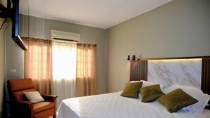 A hotel room with a bed, a chair, a window with curtains, an air conditioning unit, and a marble headboard.
