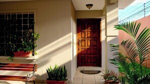 A sunlit entrance with a wooden door, potted plants, and a bench.