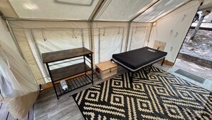 Ein Zeltraum mit einem Bett, einem kleinen Tisch und einer Aufbewahrungsbox.