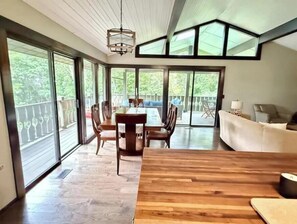 A spacious room with a wooden dining table, a sofa, and large sliding glass doors leading to an outdoor deck. - Mins to Hendersonville\Deck Views\Grill\Fireplace (Hendersonville)