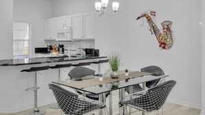 A modern kitchen with white cabinets, a black countertop, and a dining area with a glass table and wire chairs.