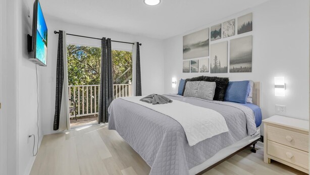A bedroom with a bed, a TV, a nightstand, and a balcony with curtains.