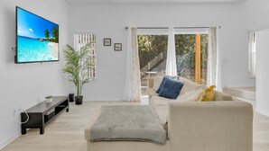 A modern living room with a flat-screen TV, a sofa, a coffee table, and a potted plant.
