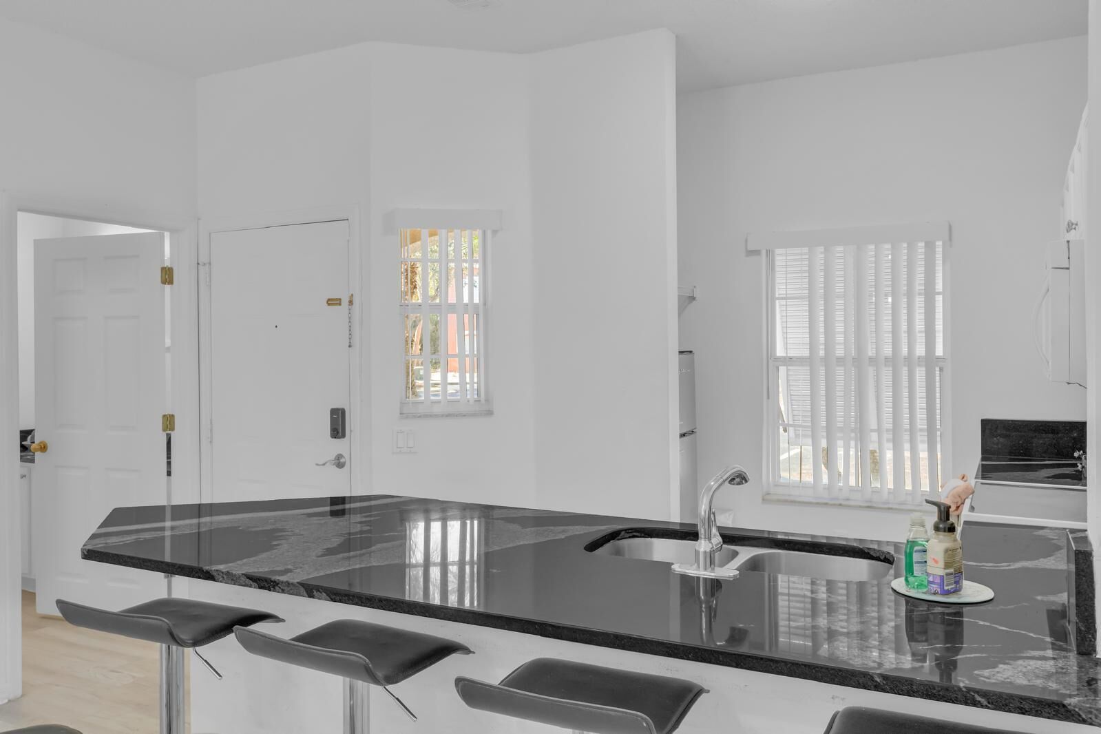 Una cocina moderna con encimera de mármol negro, pileta de acero inoxidable y taburetes de bar.