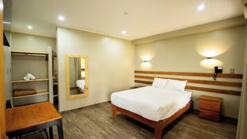 A hotel room with a wooden bed, a desk, a chair, a wardrobe, a mirror, and a nightstand.