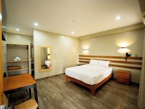 A hotel room with a wooden bed, a desk, a chair, a wardrobe, a mirror, and a nightstand.