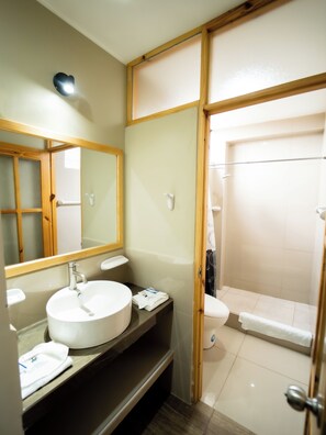 Ein Badezimmer mit Holzwaschtisch, runder Spüle, Spiegel, Toilette und Duschbereich.
