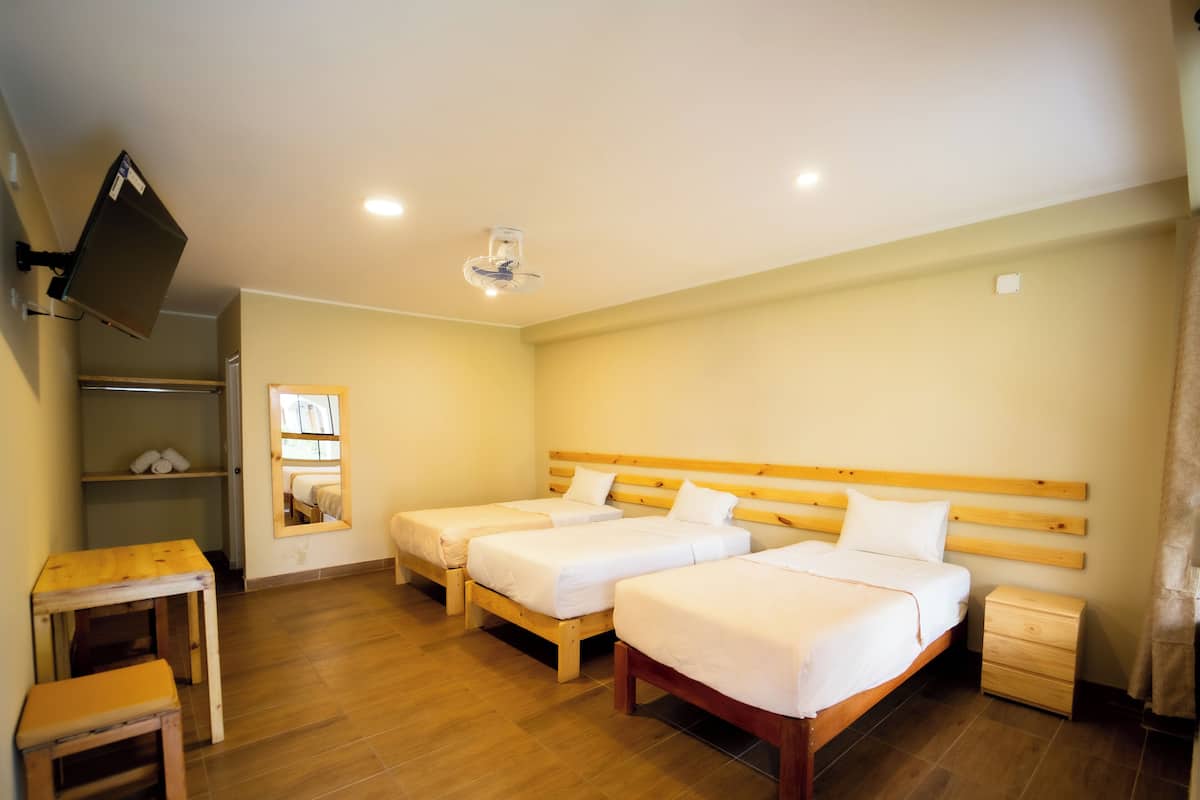 A hotel room with two single beds, a wooden nightstand, a small wooden table, a mirror, and a shelf with towels.