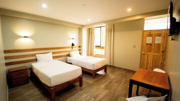 A hotel room with two single beds, a wooden desk, a chair, a nightstand, and a wooden wardrobe.