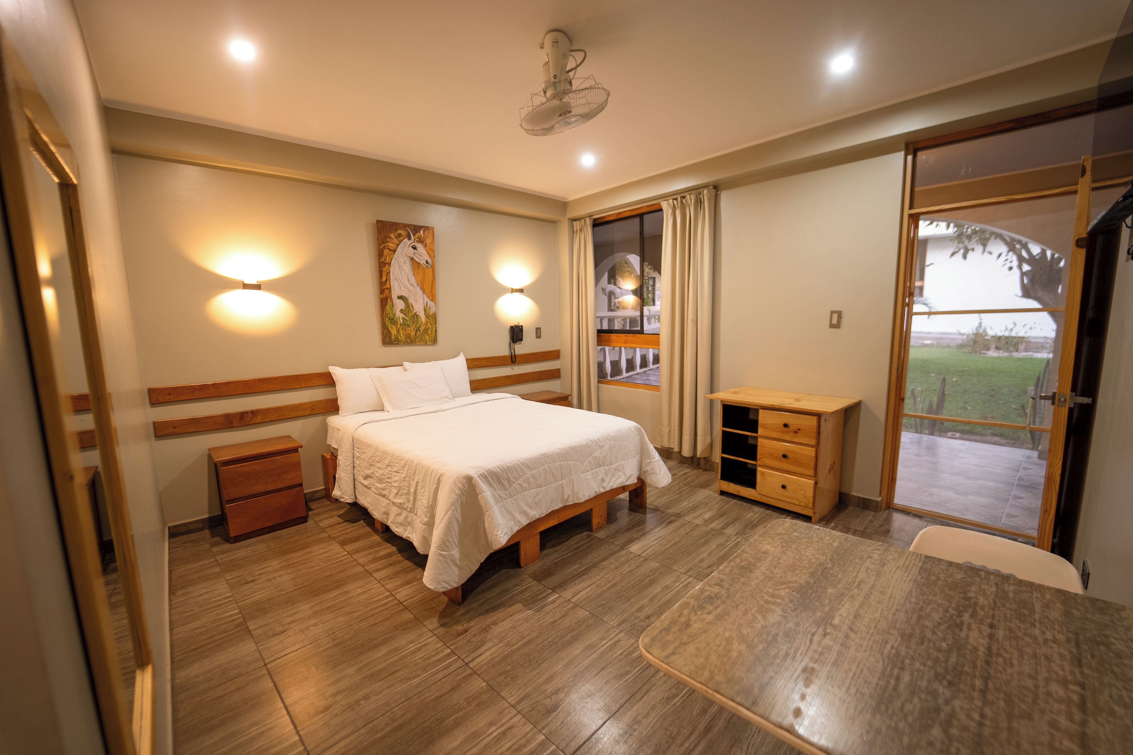 A hotel room with a bed, bedside table, and a view of the outdoors.