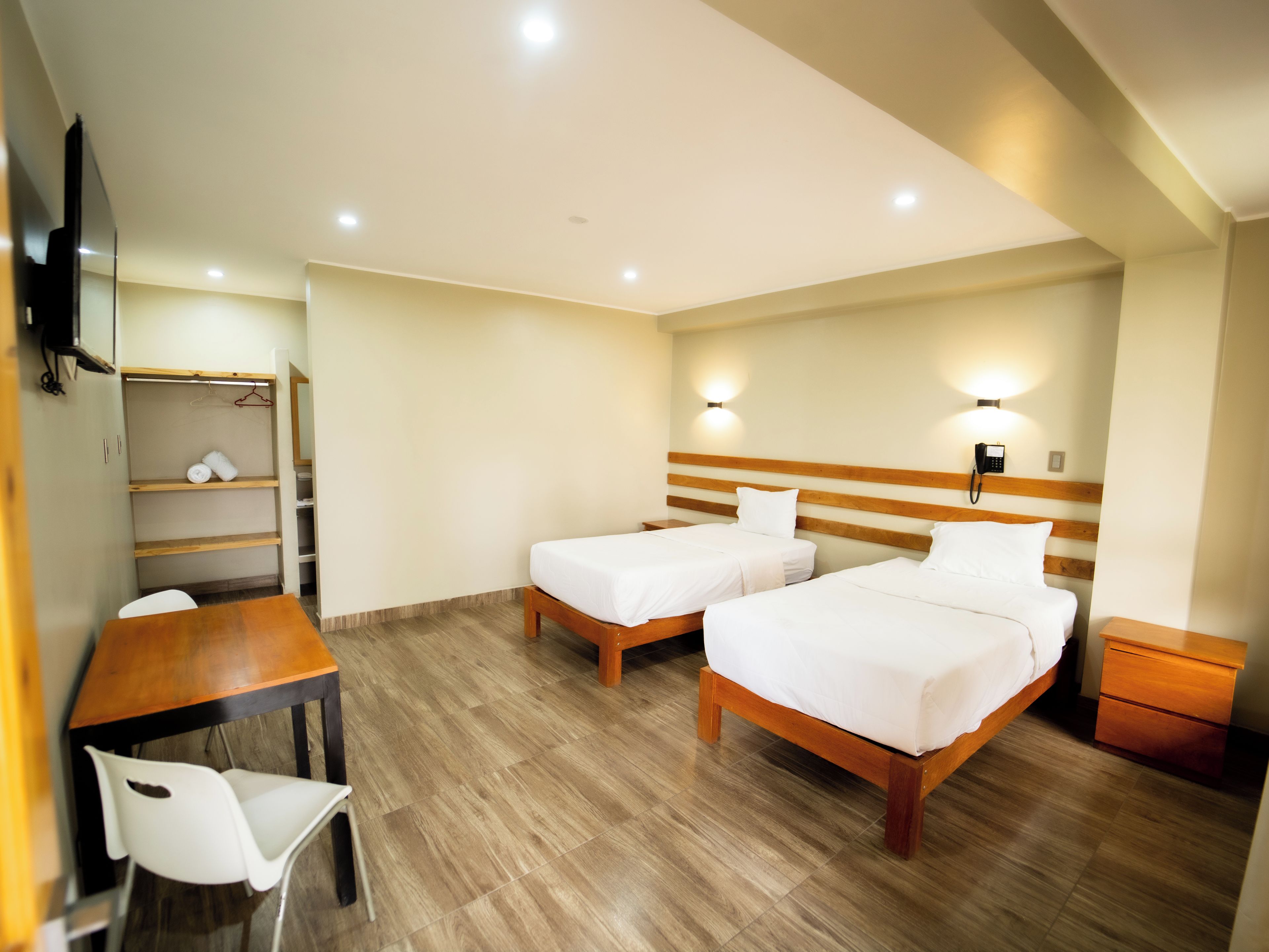 A hotel room with two beds, a wooden desk, a chair, a wardrobe, and a bedside table.