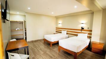 A hotel room with two beds, a wooden desk, a chair, a wardrobe, and a bedside table.