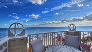 A balcony with a view of the ocean, featuring a table and chairs, and decorative metal railings.