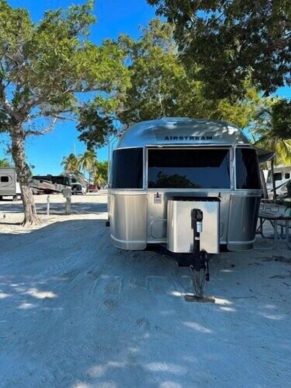Hopeanvärinen Airstream-matkailuauto on pysäköity hiekkarannalle, ja taustalla näkyy palmuja.