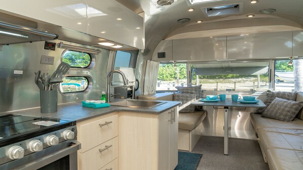 A compact RV kitchen with a stove, sink, and dining area.