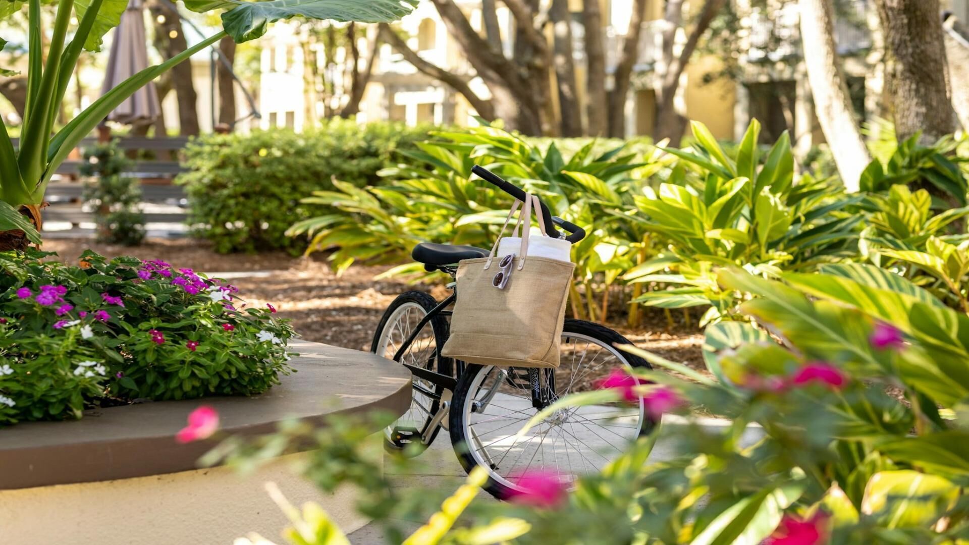 Un vélo avec un sac fixé à son porte-bagages, garé dans un jardin où poussent différentes plantes et fleurs.