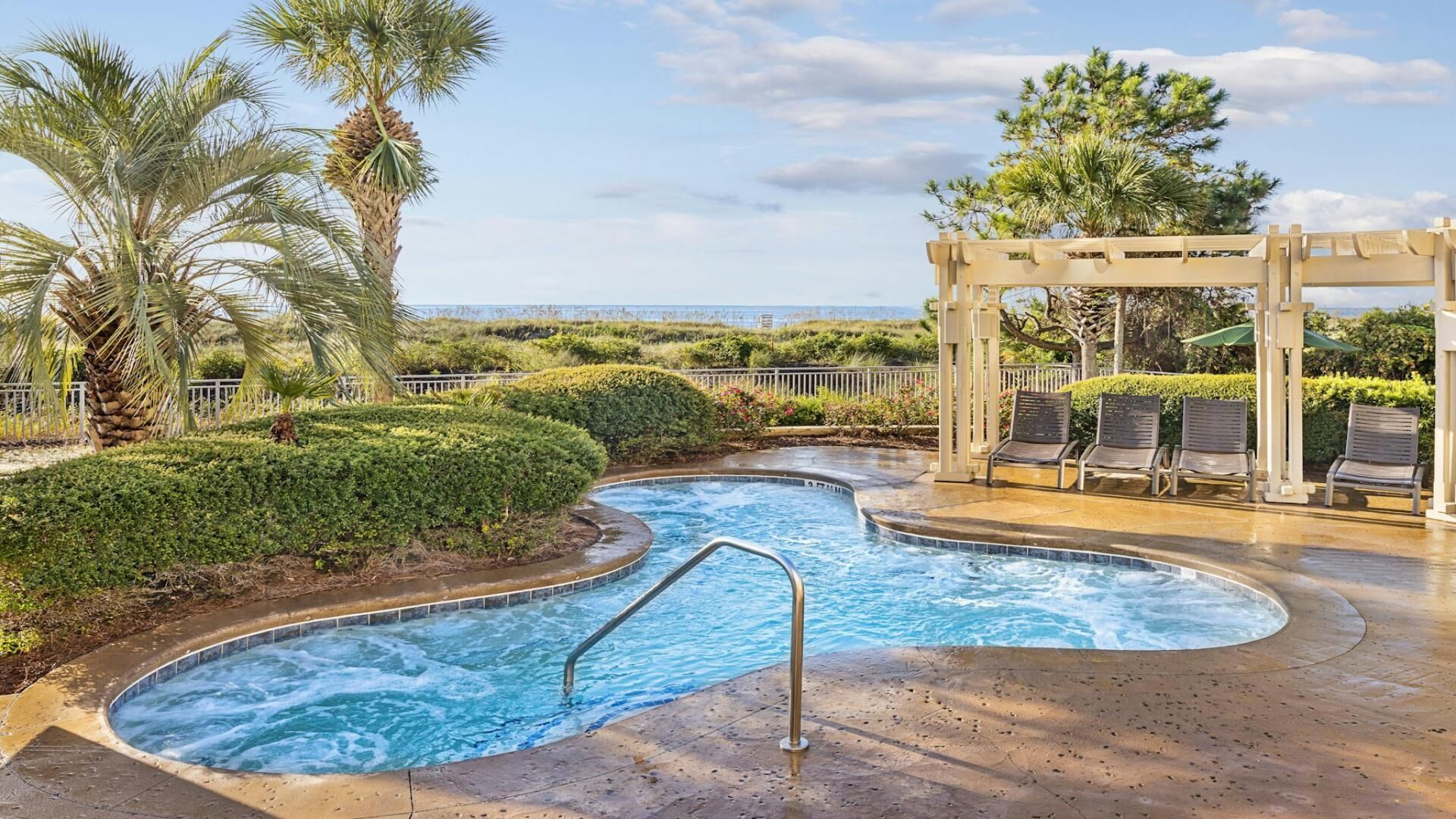 A pool area with a hot tub, lounge chairs, and a pergola.