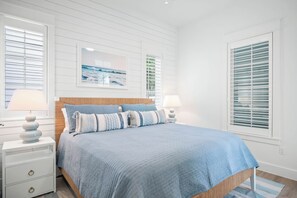 Une chambre à coucher comprenant un lit, deux tables de chevet, une commode, un tableau encadré et une fenêtre avec des stores.