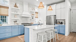 A modern kitchen with white and blue cabinetry, a large island with stools, and pendant lighting. - Birds Nest 160 Tai-f (Port Aransas)