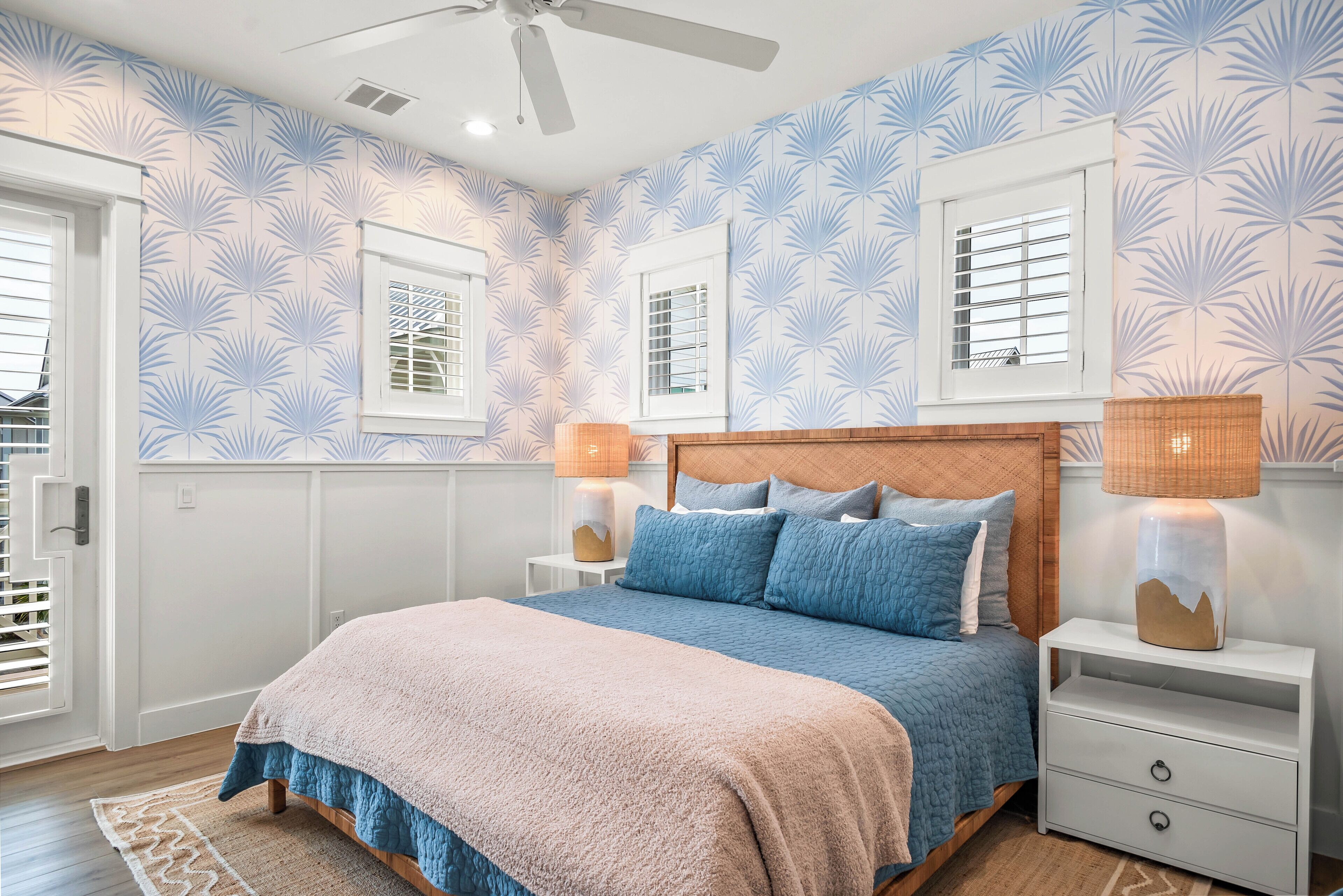 Une chambre à coucher avec un lit, des tables de chevet, un ventilateur de plafond et un papier peint à motifs.