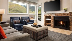 A modern living room with a fireplace, a flat-screen TV, and a view of a mountainous landscape.