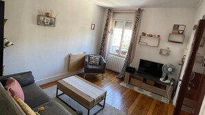 A living room with a sofa, a coffee table, a TV, and a chair. There is a window with curtains and a door leading to another room. - Nice 2 rooms, cosy, quiet - Near forest - Near Paris ! (Sèvres)