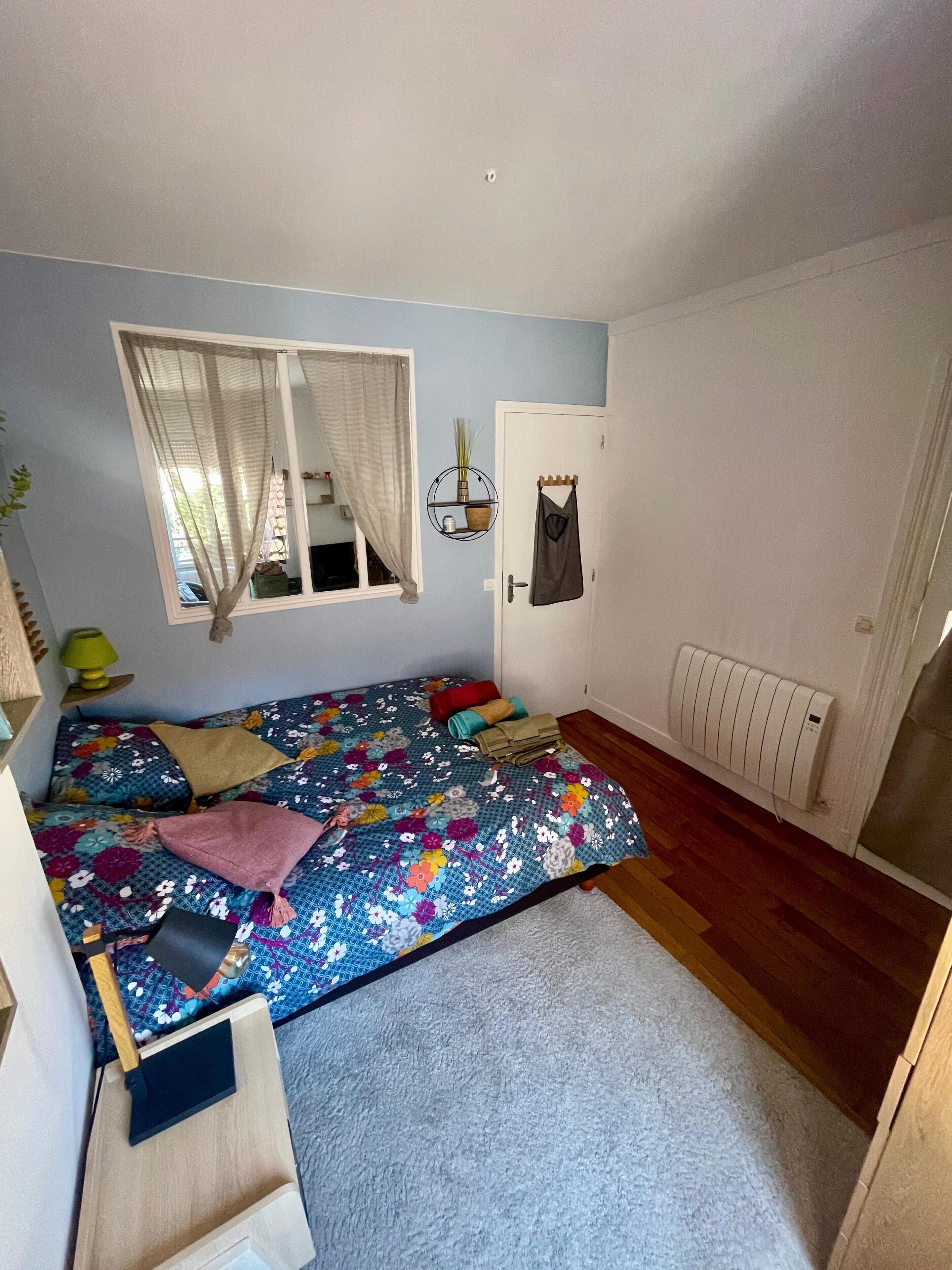 Een slaapkamer met een bed, een raam met gordijnen, een radiator en een deur.