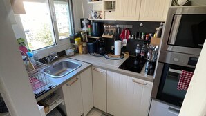 A compact kitchen with white cabinets, a stainless steel oven, and a window providing natural light. - Nice 2 rooms, cosy, quiet - Near forest - Near Paris ! (Sèvres)