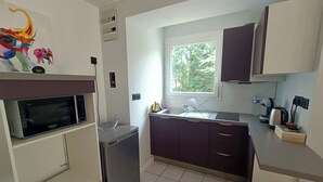Een kleine keuken met een magnetron, koelkast, spoelbak en kastjes.