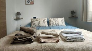 Een netjes opgemaakt bed met meerdere kussens en opgevouwen handdoeken. Er hangen wandlampen en kunstwerken boven het bed.