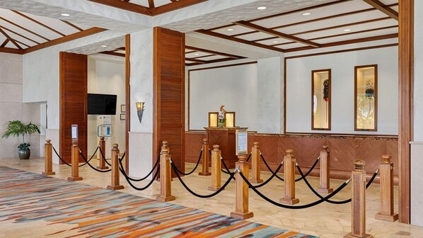 Un hall d’hôtel comprenant un comptoir d’accueil, des colonnes en bois, une moquette à motifs et un écran de télévision.