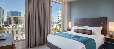 Habitació d'hotel amb un llit gran, vistes a la ciutat i un escriptori amb una làmpada.