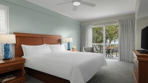Habitación de hotel con una cama grande, dos mesitas de noche con lámparas, un televisor y un balcón con mesa y sillas.