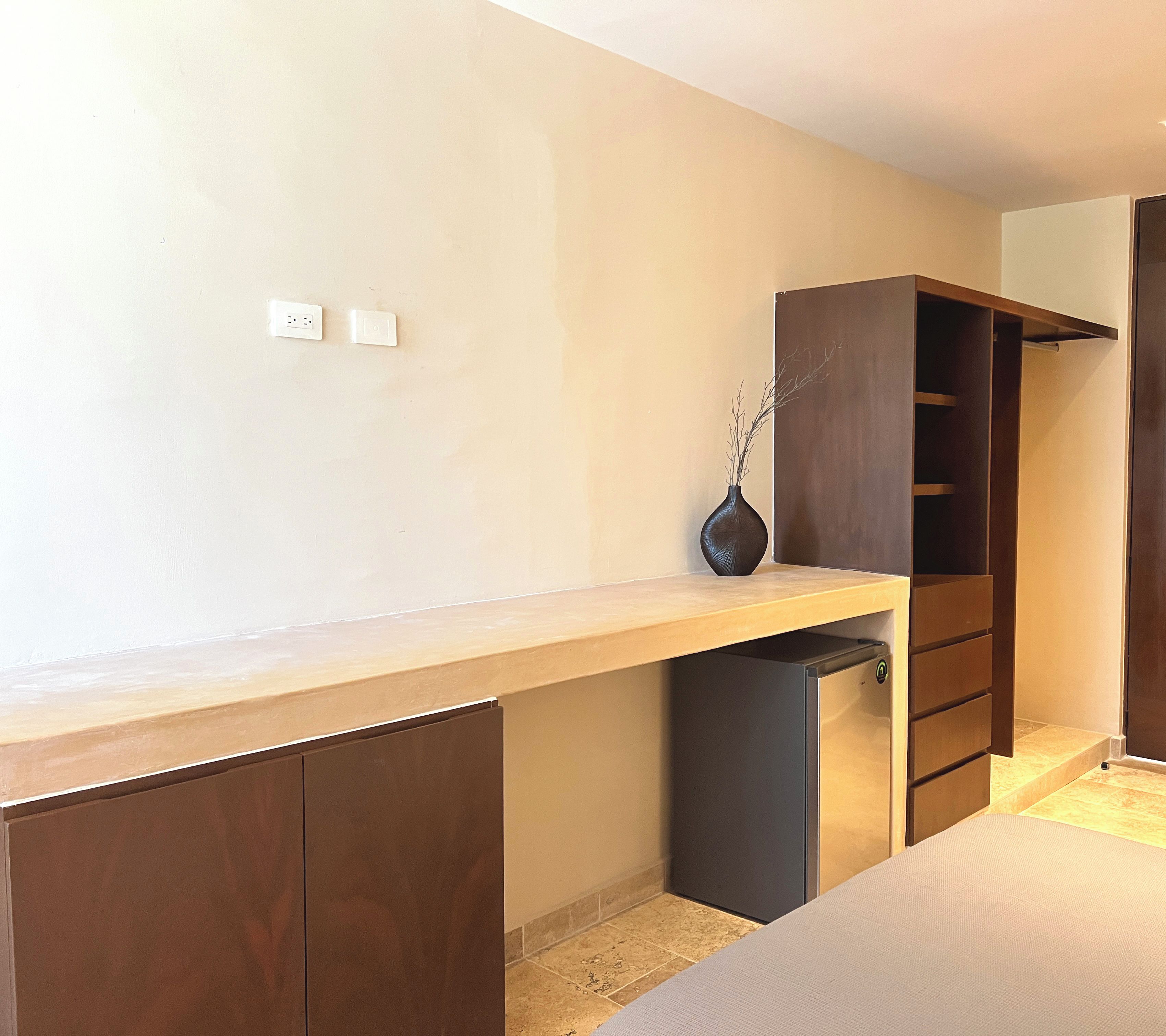 Un dormitorio con cama, armario de madera, escritorio pequeño y un jarrón con ramas.
