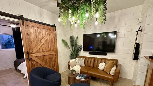 A living room with a sliding barn door, a brown leather sofa, two dark blue armchairs, a coffee table with a magazine, and a TV mounted on the wall. - 4 Min Walk to Beach & Restaurants (Manhattan Beach)