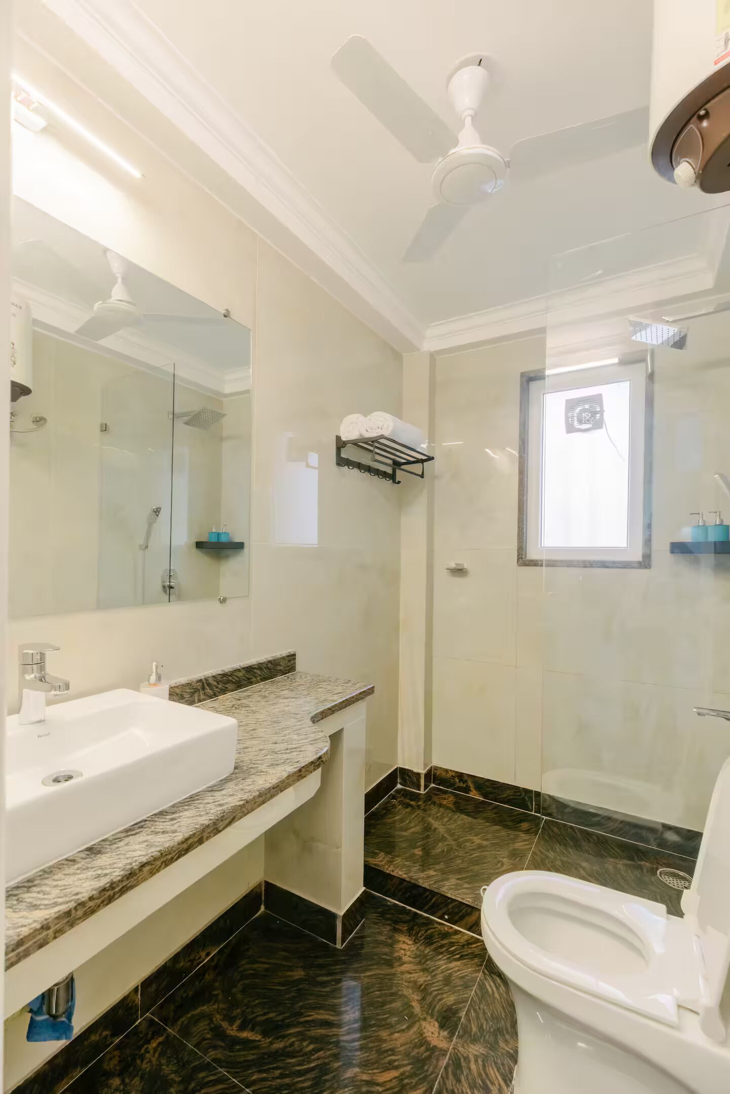 Un baño con un lavamanos blanco, cabina de ducha con mampara de vidrio, inodoro y ventilador de techo.