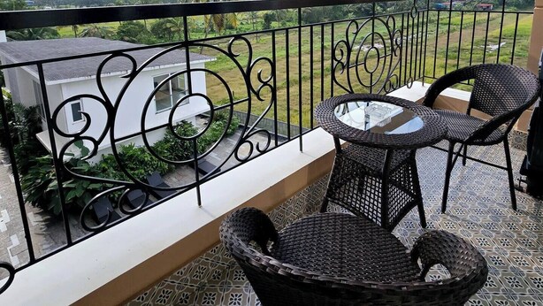 Un balcon donnant sur un paysage verdoyant, un bâtiment blanc et une table avec des chaises.