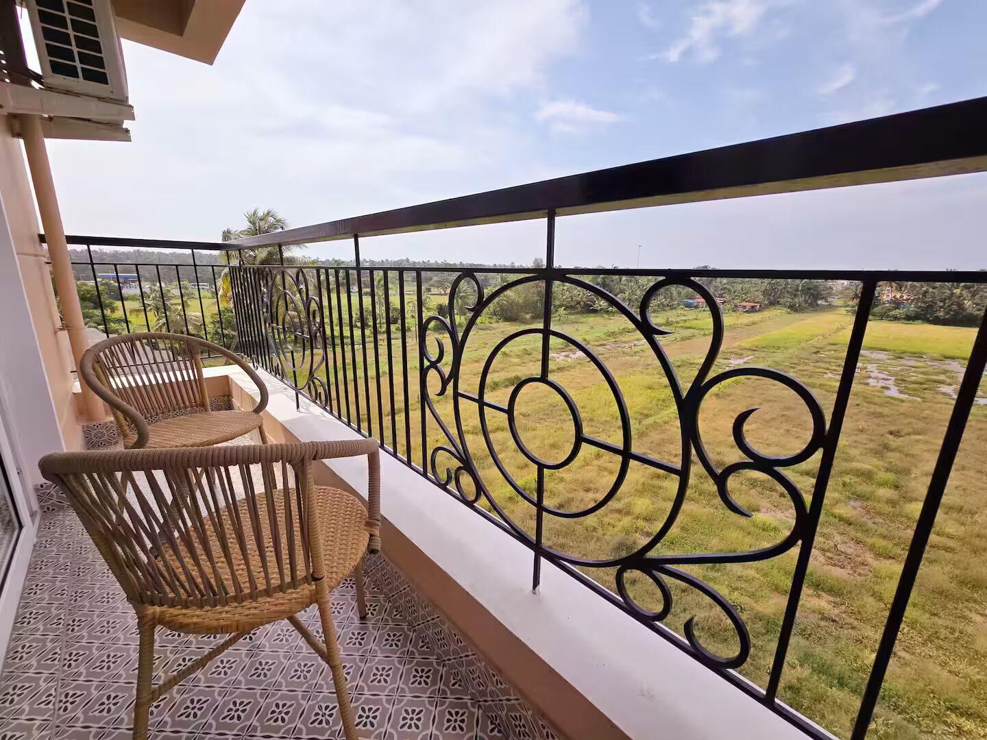 A balcony with a wrought iron railing, two wicker chairs, and a view of a green landscape.