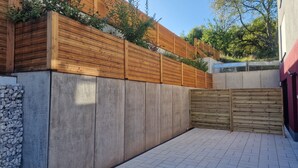 Un espace extérieur moderne avec un mur en béton, une clôture en bois et un sol carrelé.
