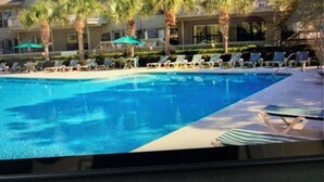 Una piscina con sillones de descanso y palmeras.