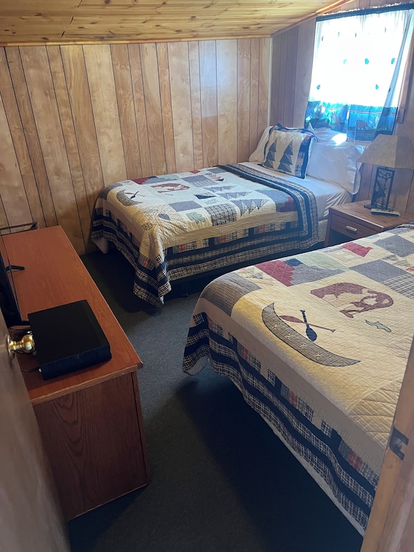 A room with two beds, a wooden desk, and a window with curtains. - Pioneer Motel (West Yellowstone)