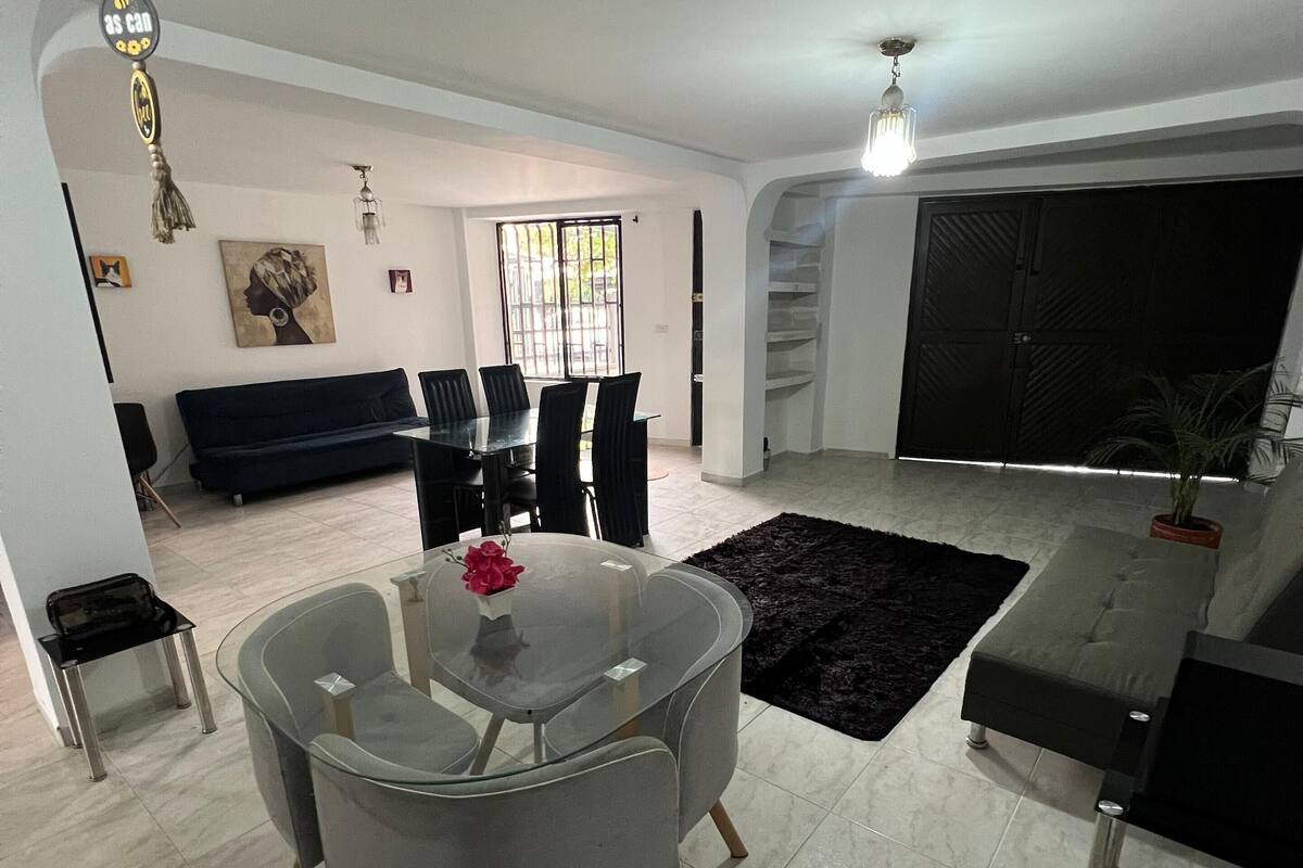 Una sala moderna con una mesa de comedor de vidrio, sofás grises y una alfombra negra.