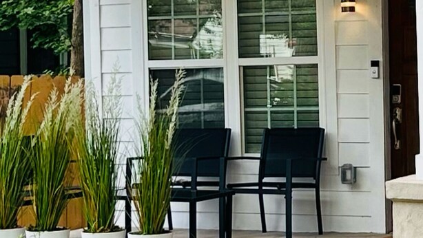 Una casa con porche, dos sillas y plantas en macetas.