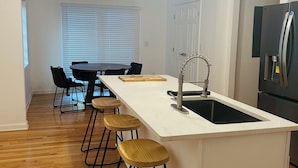 Una cocina moderna con una isla central, taburetes de bar, un refrigerador e iluminación colgante.