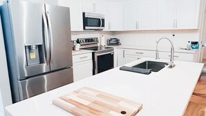 Una cocina moderna con armarios blancos, electrodomésticos de acero inoxidable y una tabla de cortar de madera sobre la encimera.